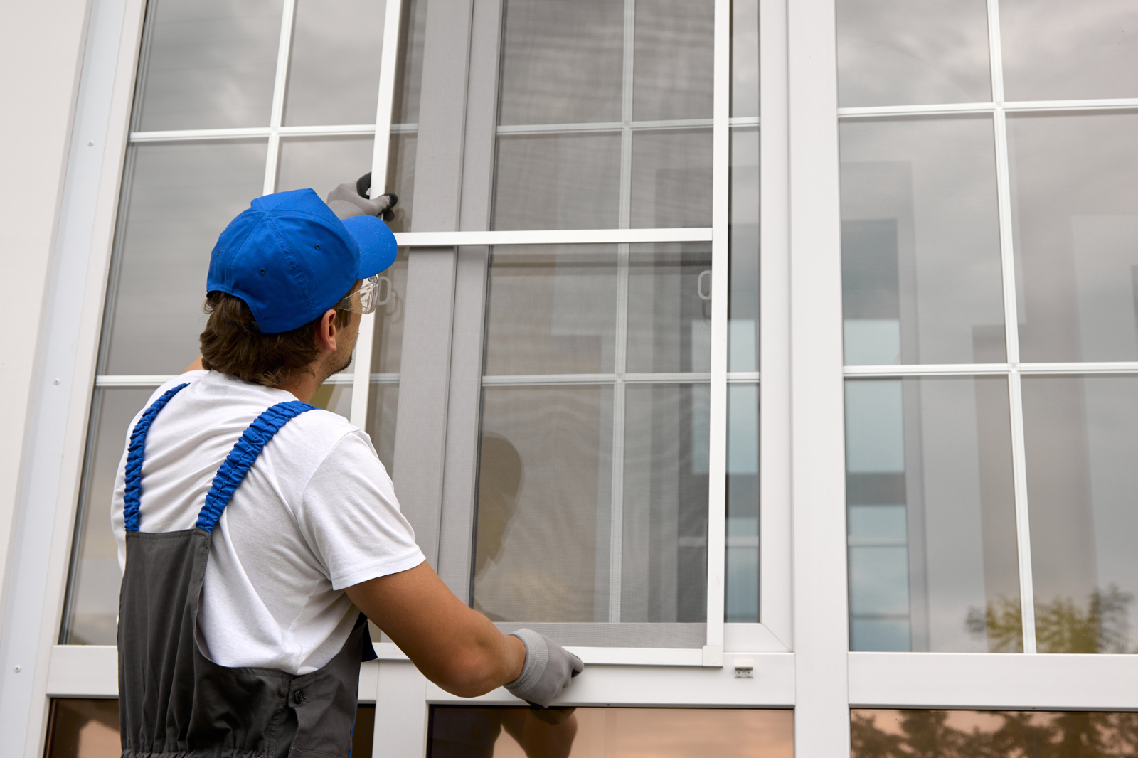 Een installateur monteert een vliegenraam op een wit PVC-raam in een moderne woning.