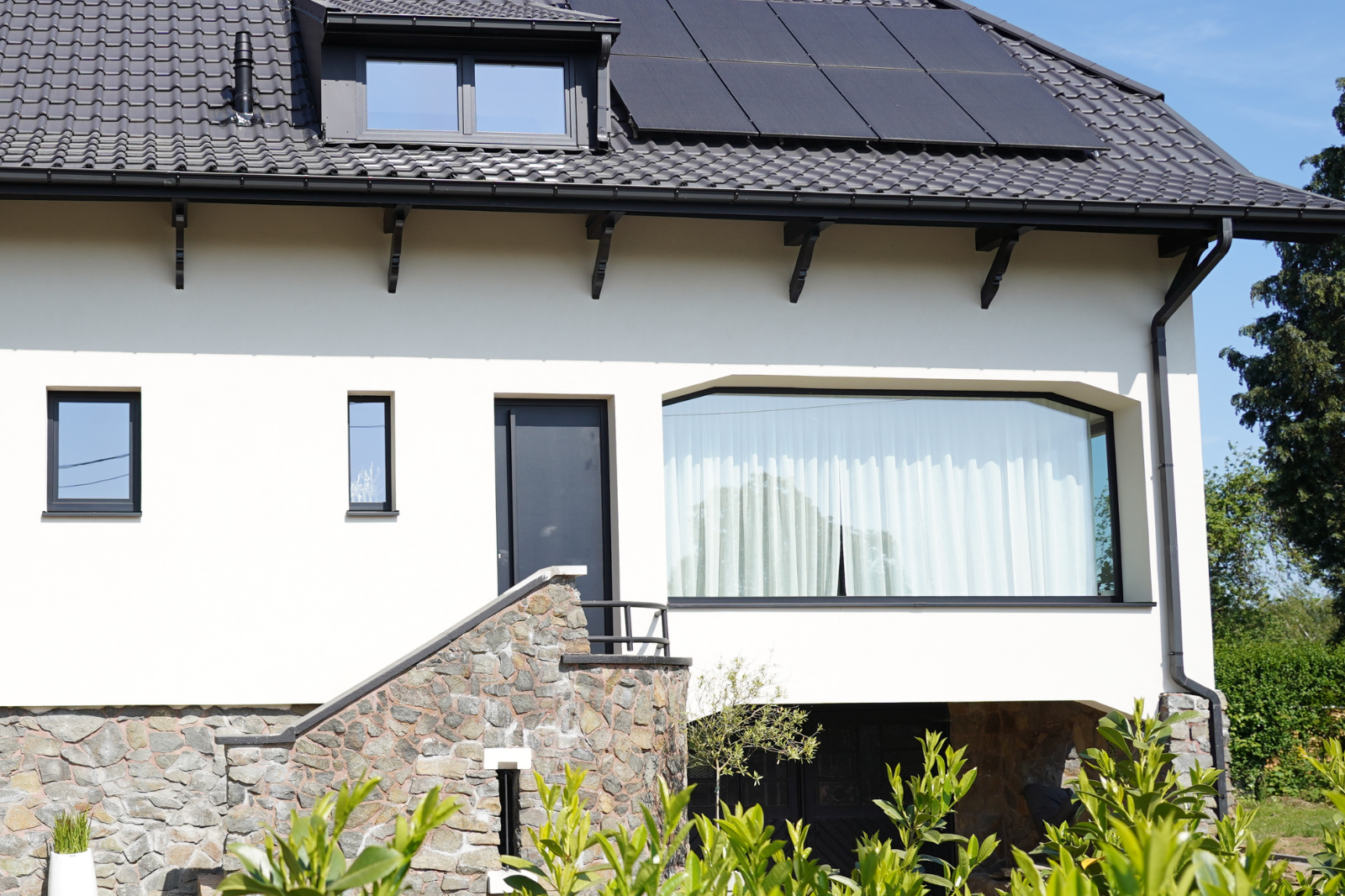 Woning met zwarte aluminium ramen en voordeur, zichtbaar vanop afstand