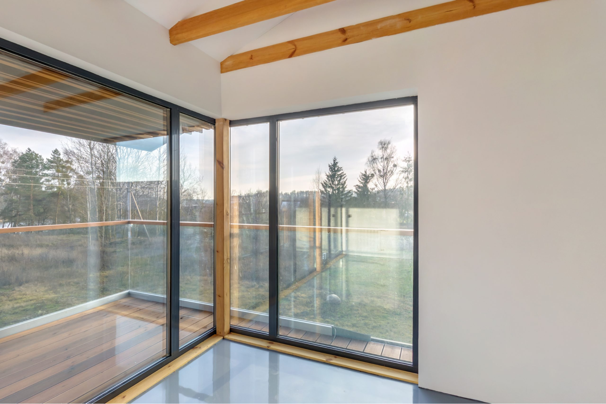 Hoekruimte met grote glaspartijen en houten balkenplafond, met uitzicht op balkon en groene omgeving.
