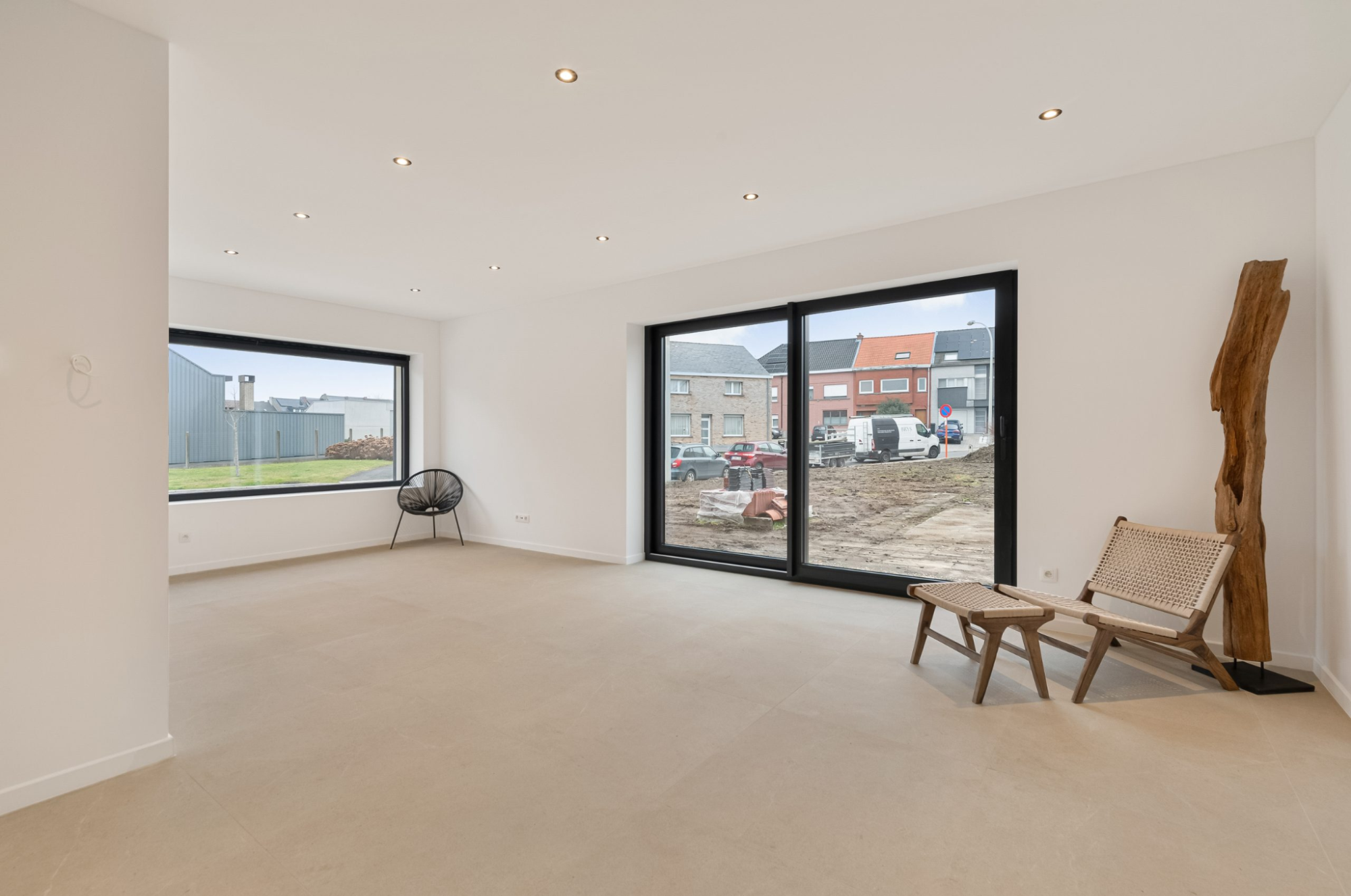 Moderne, lichte woonkamer met grote raampartijen en schuifdeur naar buiten, minimalistisch ingericht met houten stoel en uitzicht op straat