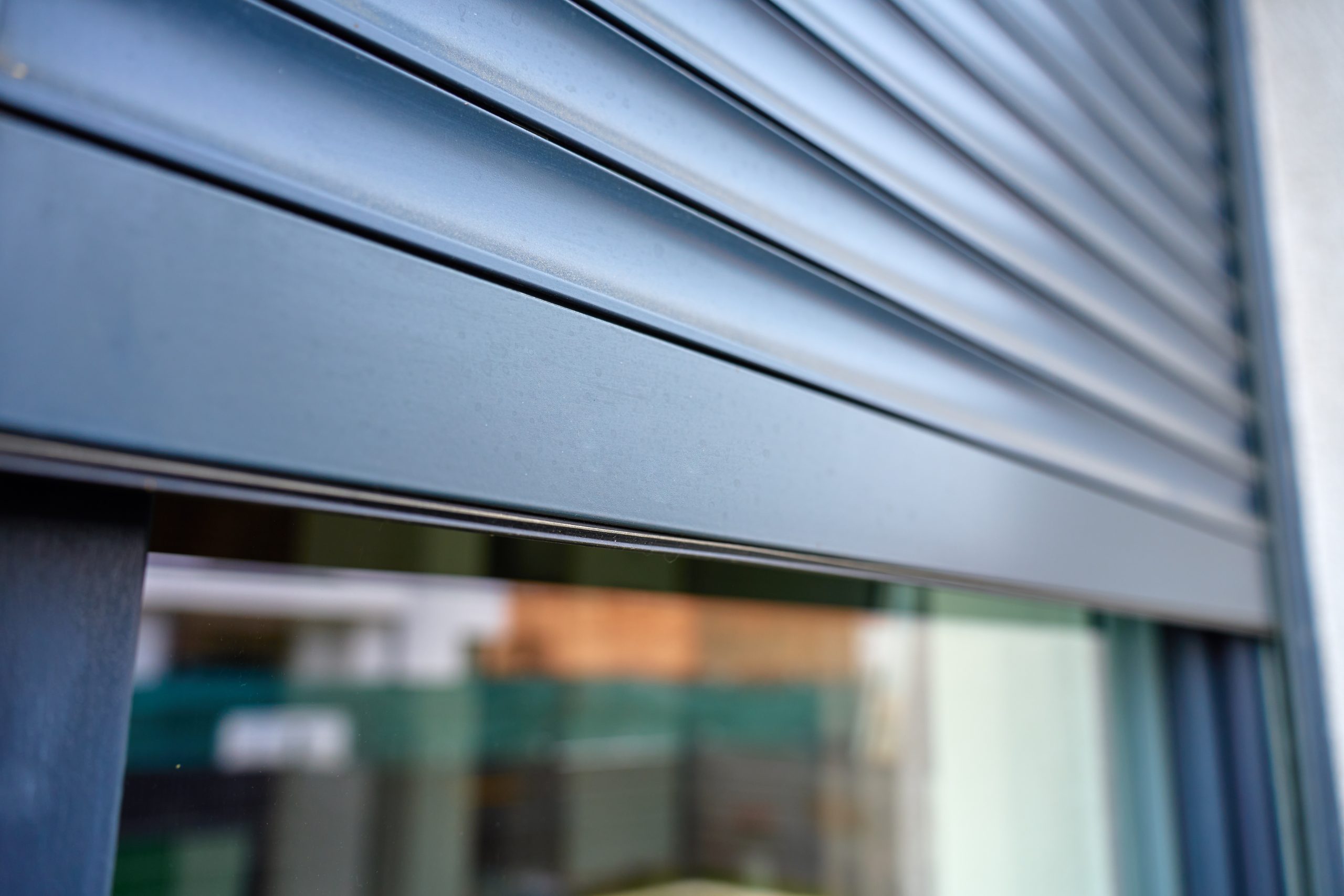 Close-up van de lamellen van een antraciet aluminium rolluik, half neergelaten voor een raam.