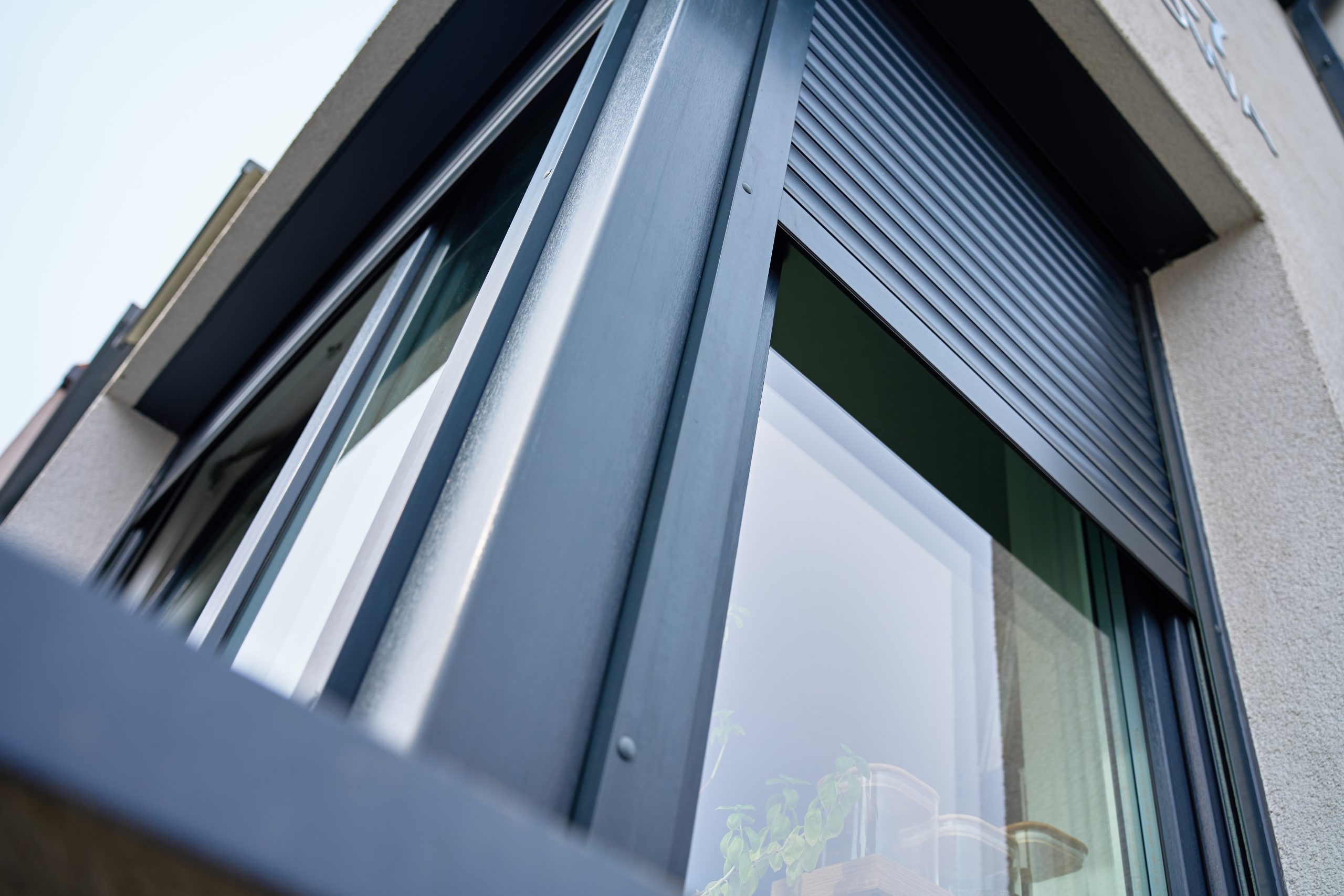 Antraciet aluminium opbouwrolluiken half neergelaten op grote ramen van een moderne woning